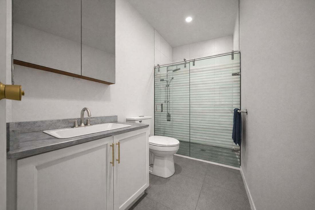 Baño con ducha de vidrio. Mueble de lavamanos y acabados claros.