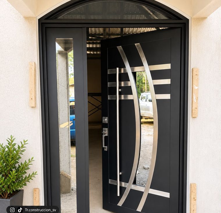 Puerta negra con franjas curvas de acero inoxidable y tragaluz en arco de medio punto, con panel lateral de vidrio