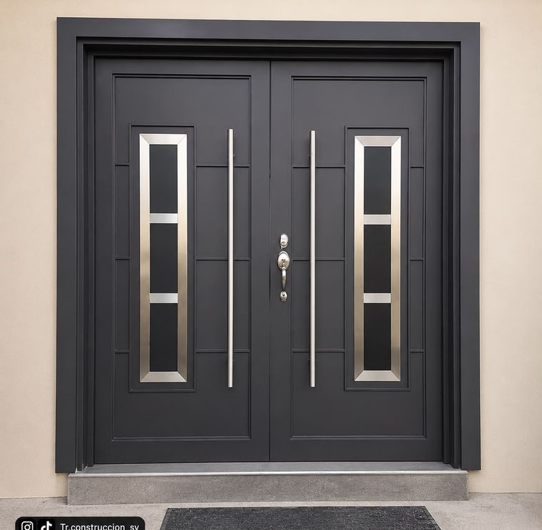Puerta gris oscuro de doble hoja con vitrales verticales enmarcados en acero inoxidable y molduras rehundidas